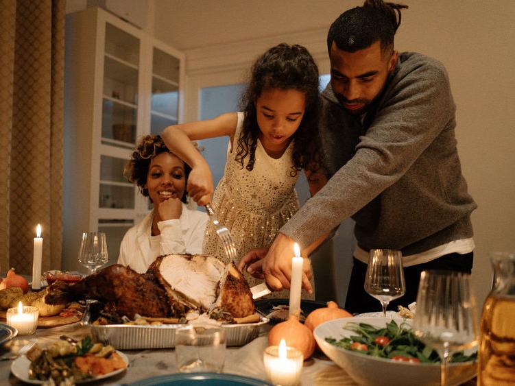 Father, child, mother carve a turkey at Thanksgiving